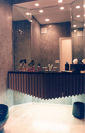 Floating vanity with a pleated dark front and black countertop below a mirrored wall