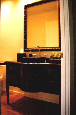 Dark furniture-style vanity with curved legs below a large carved frame mirror