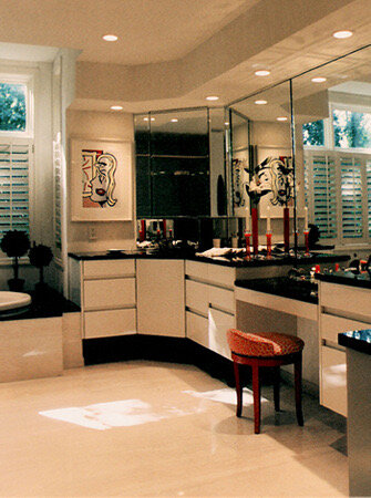 Bathroom with white vanity cabinets, black countertops, a makeup desk, and mirrored walls