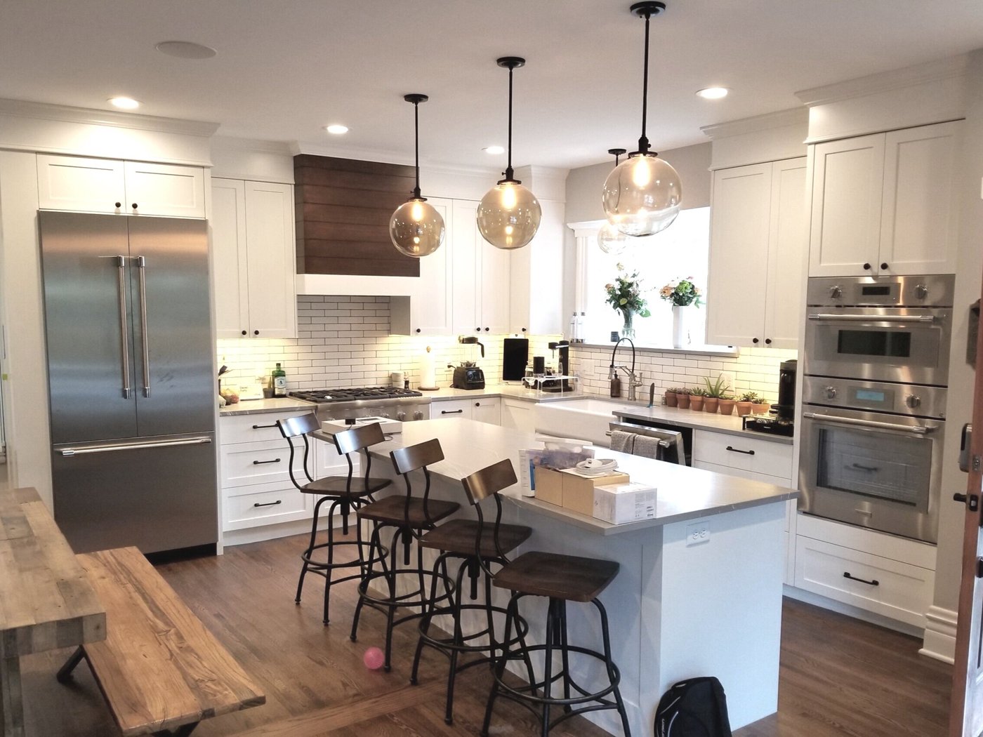 White custom kitchen cabinetry with a wood range hood, glass pendant lights, and a large island