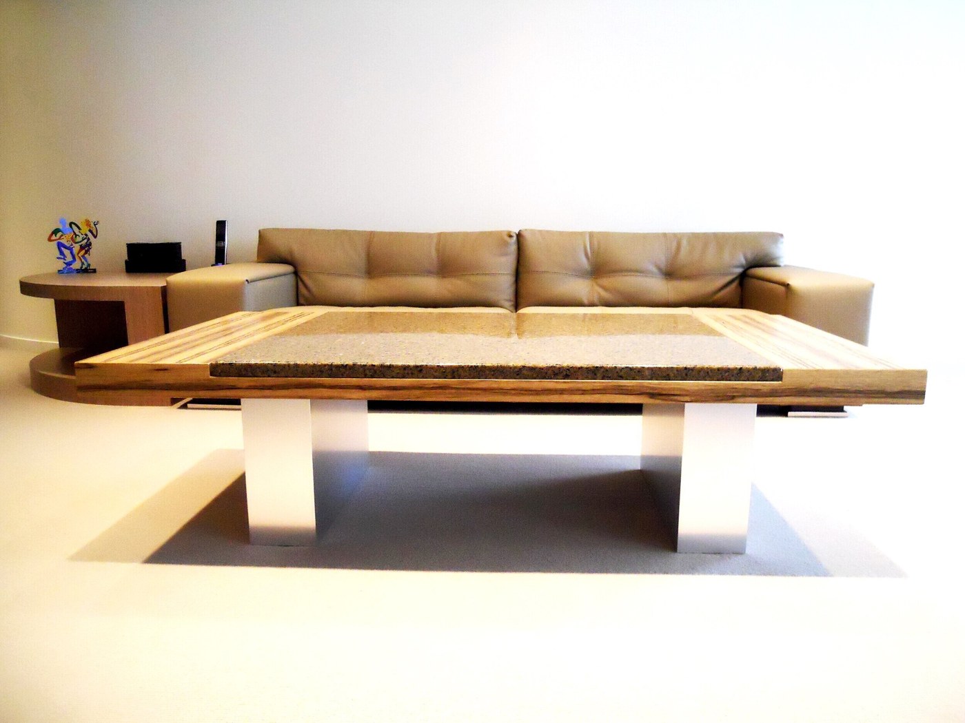 Custom coffee table with a granite inlay set into a striped wood top on brushed metal legs, in front of a leather sofa