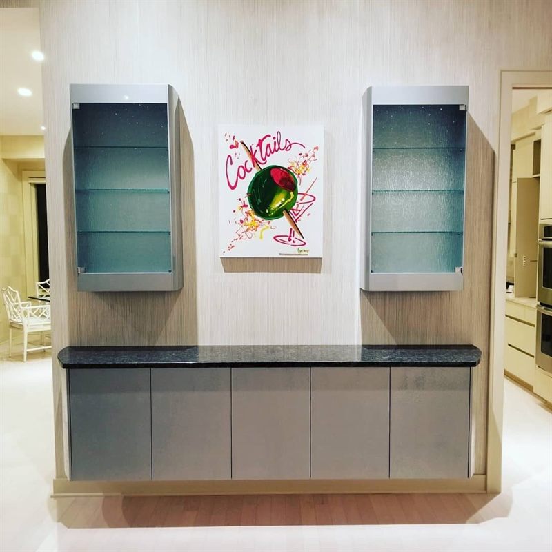 Bar wall with a gray base cabinet and two glass-front wall cabinets flanking a painting