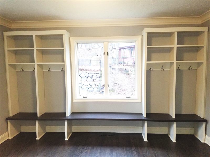 Mudroom window seat with a dark-wood bench between white open lockers with hooks