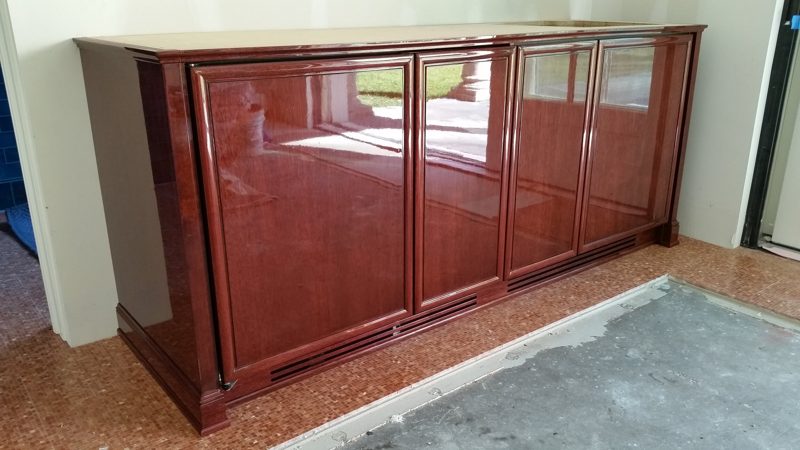 Angled view of glossy red cherry bar cabinets on an unfinished floor