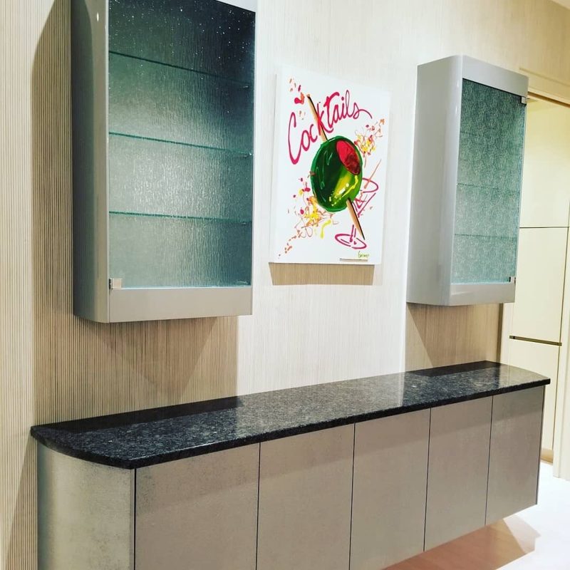 Floating gray bar cabinet with a dark granite top below two glass wall cabinets