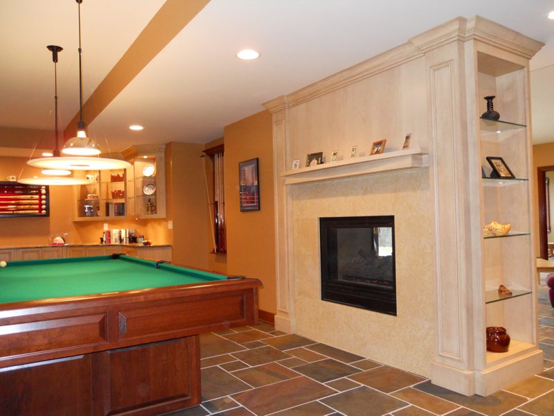 Plaster fireplace wall with lit side shelves beside a pool table