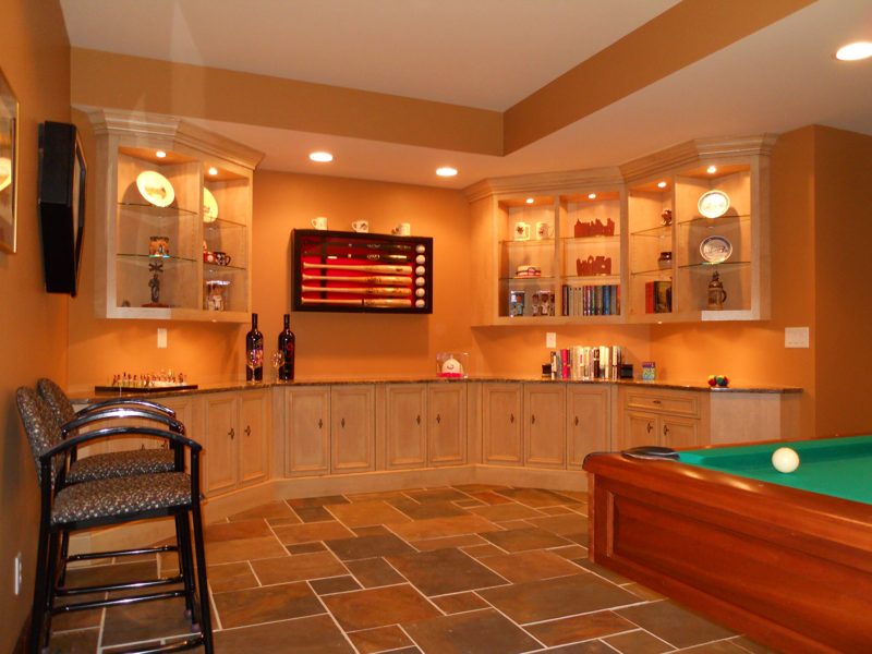 Basement bar with lighted glass-front cabinets and a tall bar stool