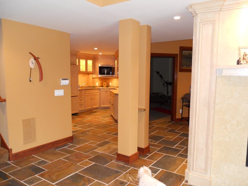 Open lower level with columns leading to a lit bar kitchen
