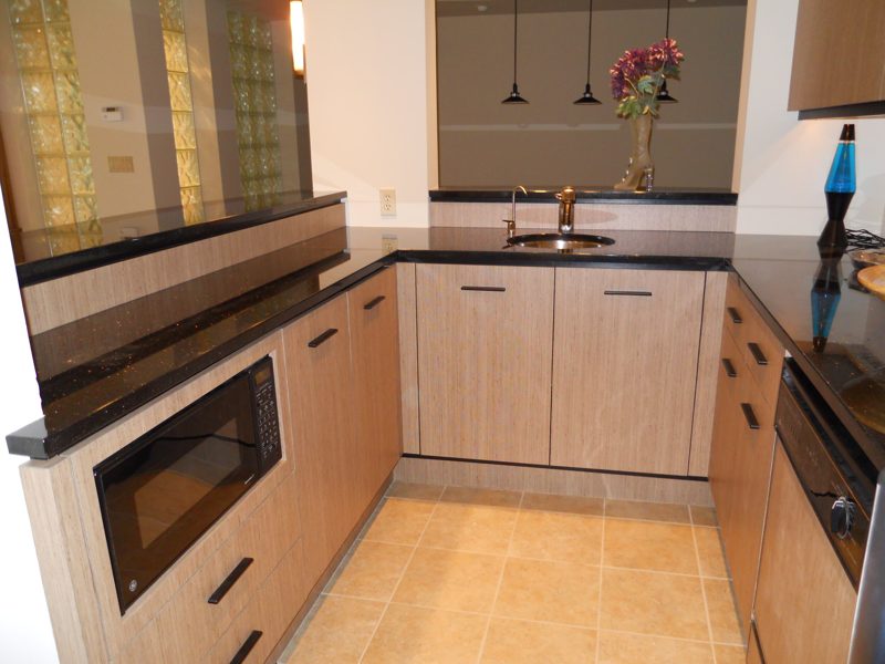 Light wood-grain bar kitchen with black counters and a built-in microwave