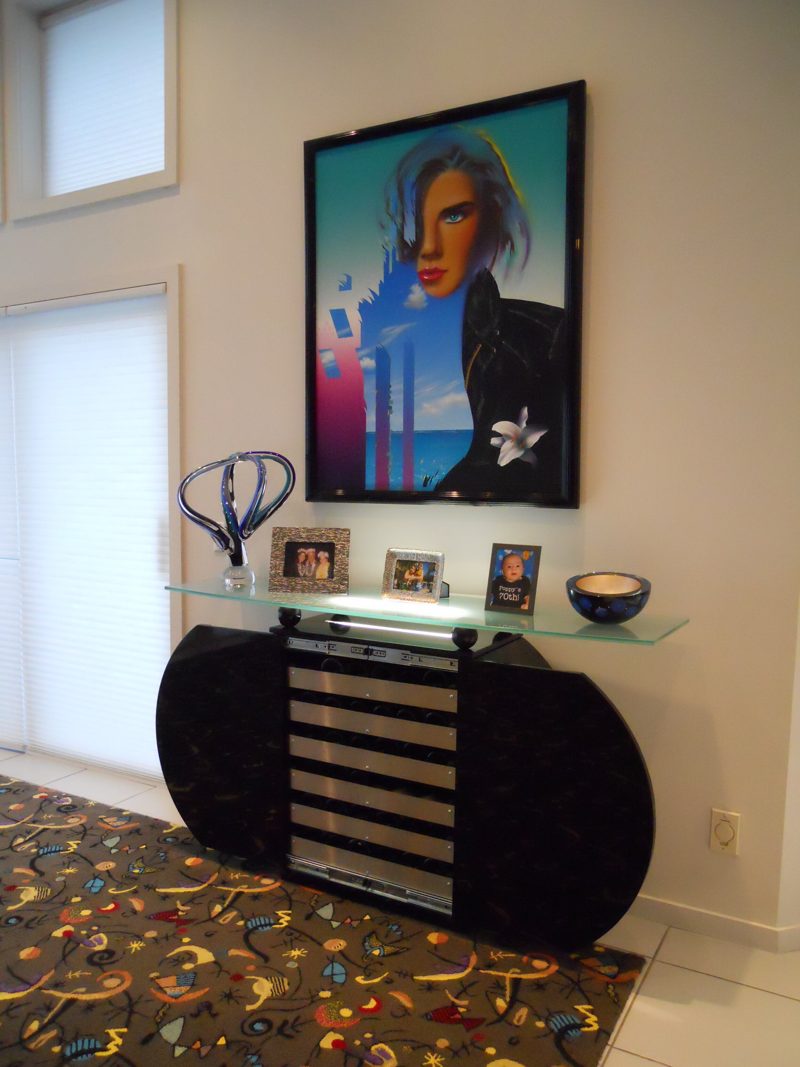 Black half-round cabinet with a wine fridge and glass shelf below art
