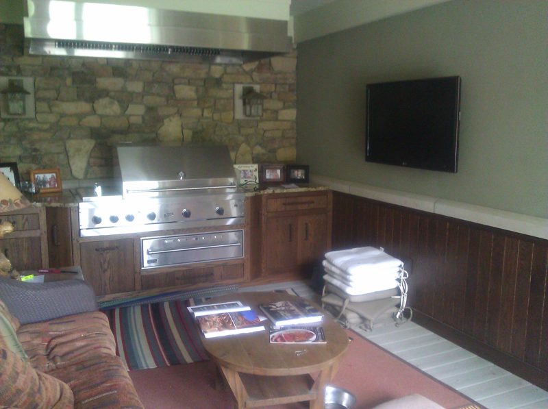 Stone wall outdoor kitchen with dark wood cabinets and a mounted TV