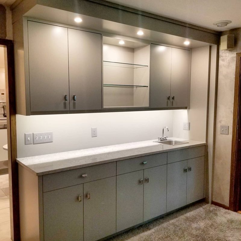Gray bar cabinetry with a lit open glass shelf and white backsplash