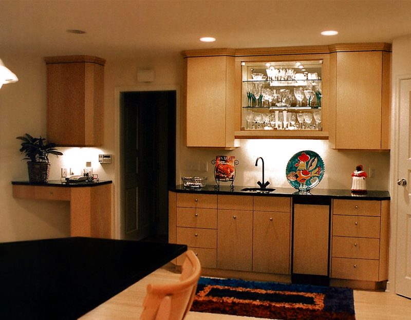 Light wood bar with glass-front upper cabinets and a dark counter