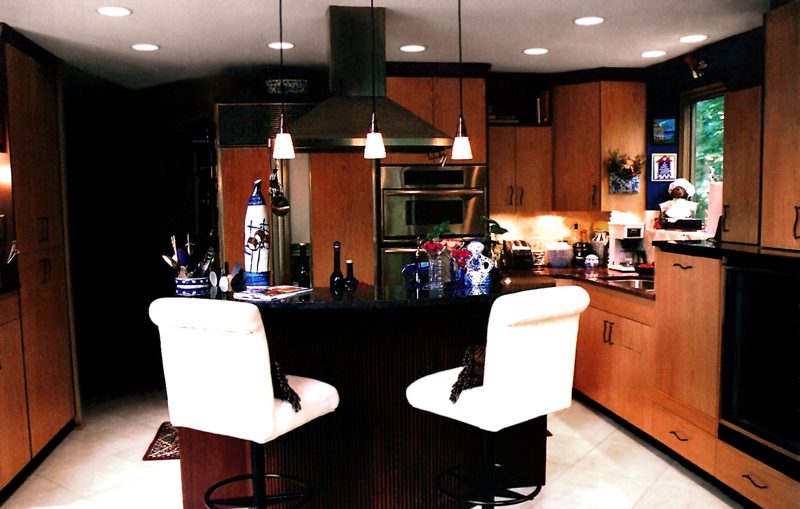 Dark island bar with white stools under pendant lights in a wood kitchen