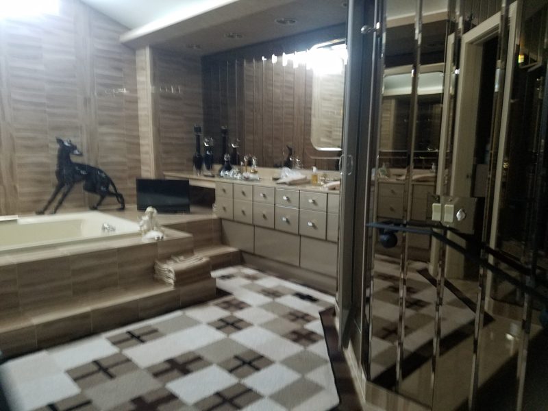 Bathroom with a sunken tub, cream drawer vanity, and mirrored wall panels