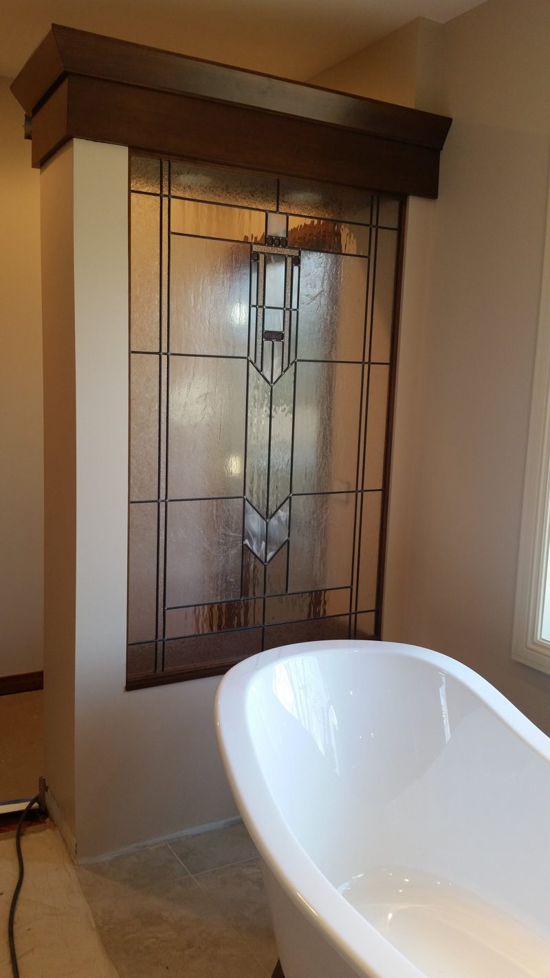 Dark wood tower with a leaded glass panel beside a freestanding tub