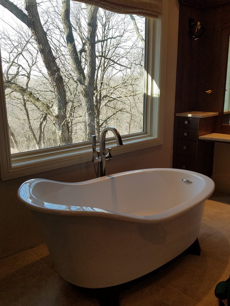Freestanding white tub below a window beside dark wood cabinetry