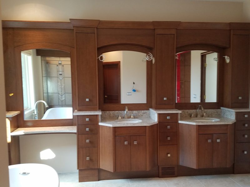 Dark wood double vanity with arched mirrors, raised panel drawers, and a makeup desk