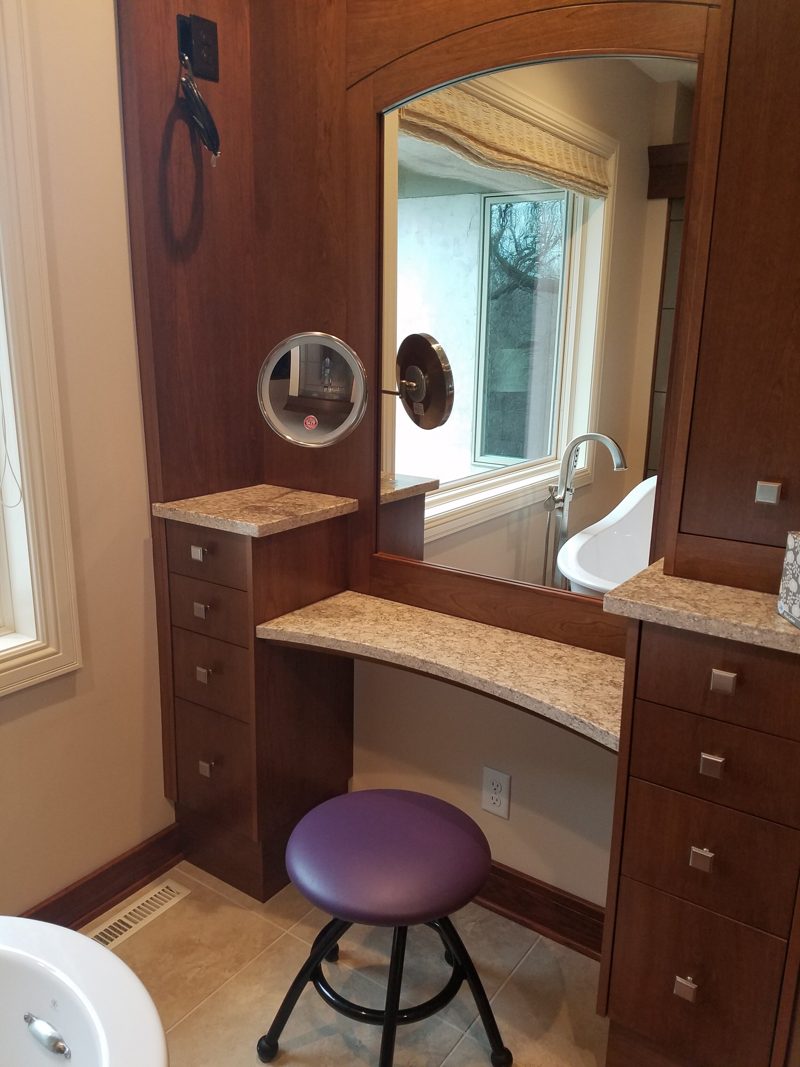 Dark wood makeup desk with a stone top between drawer towers and an arched mirror