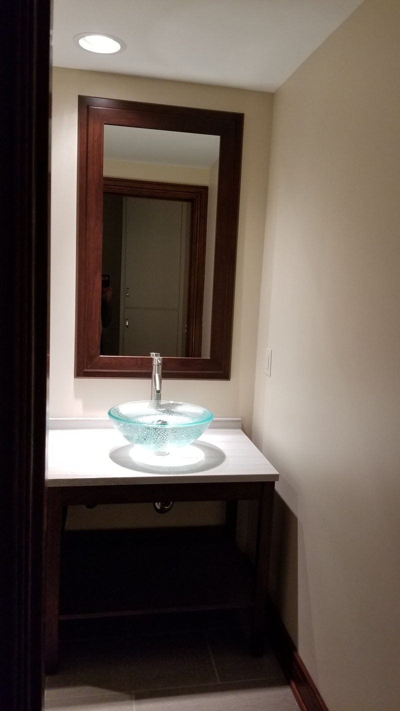 Open dark wood vanity with a glass vessel sink and a framed mirror