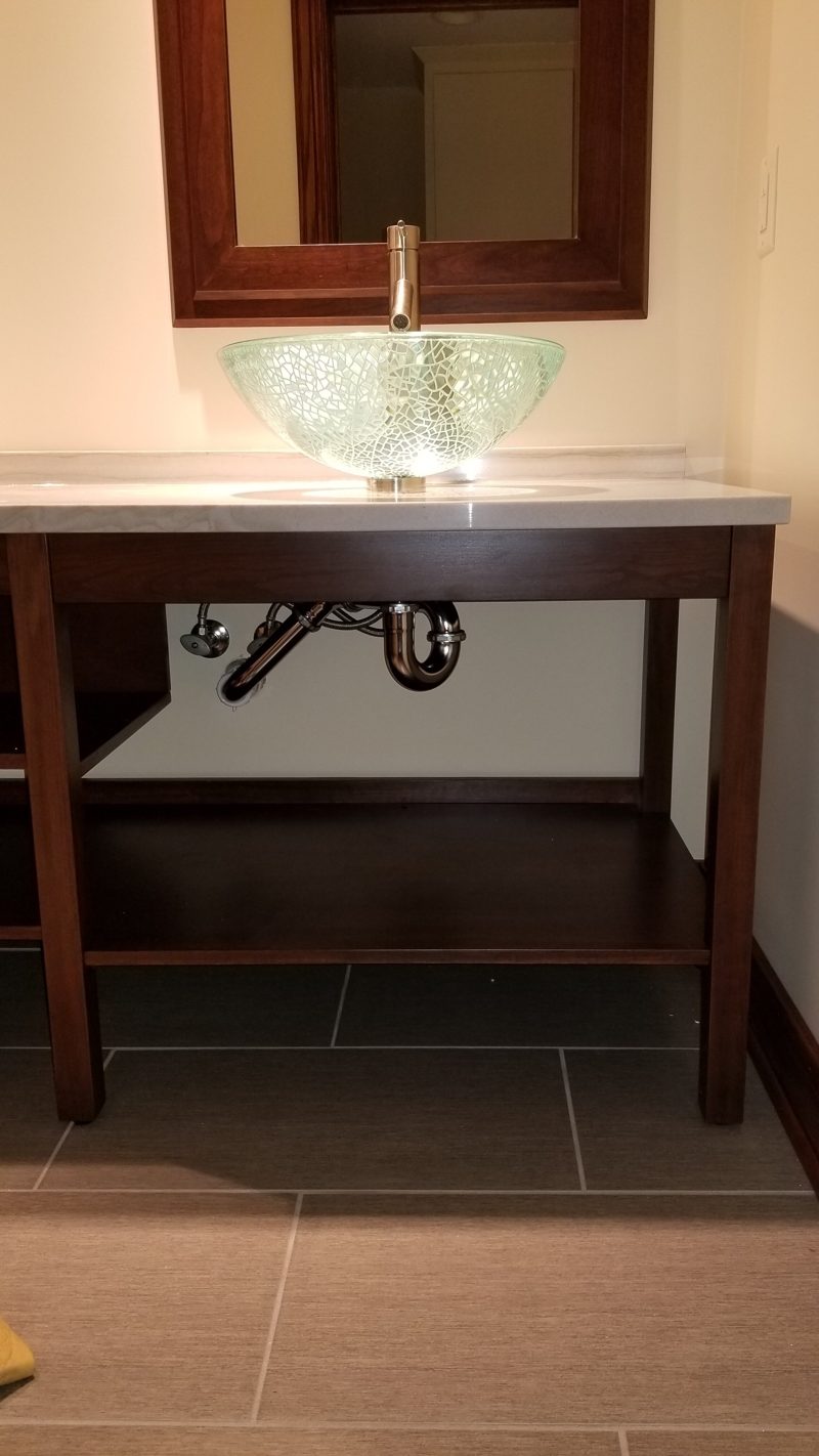 Dark wood console vanity with open base, glass vessel sink, and exposed drain