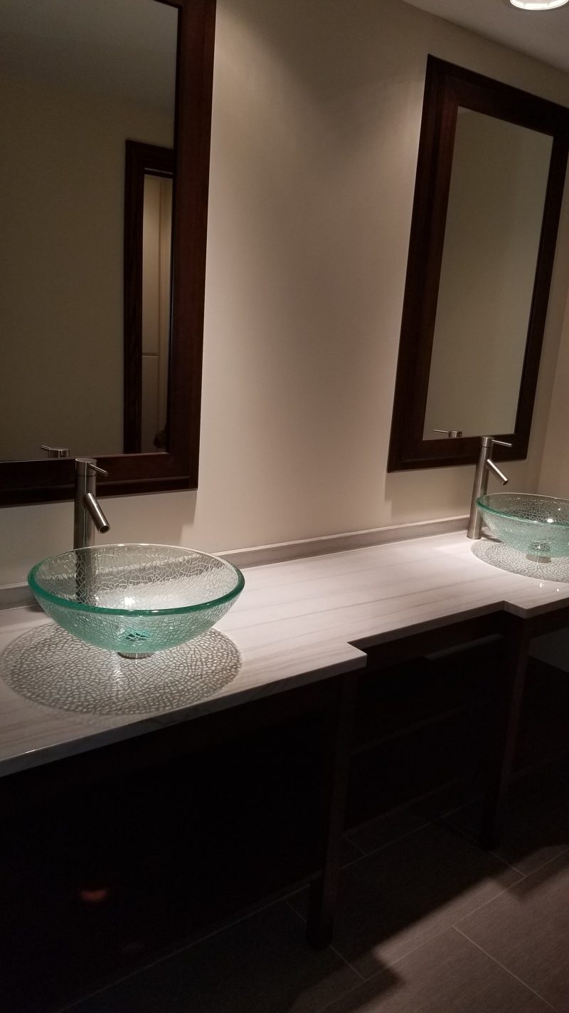 Double vanity with glass vessel sinks, white top, and dark framed mirrors
