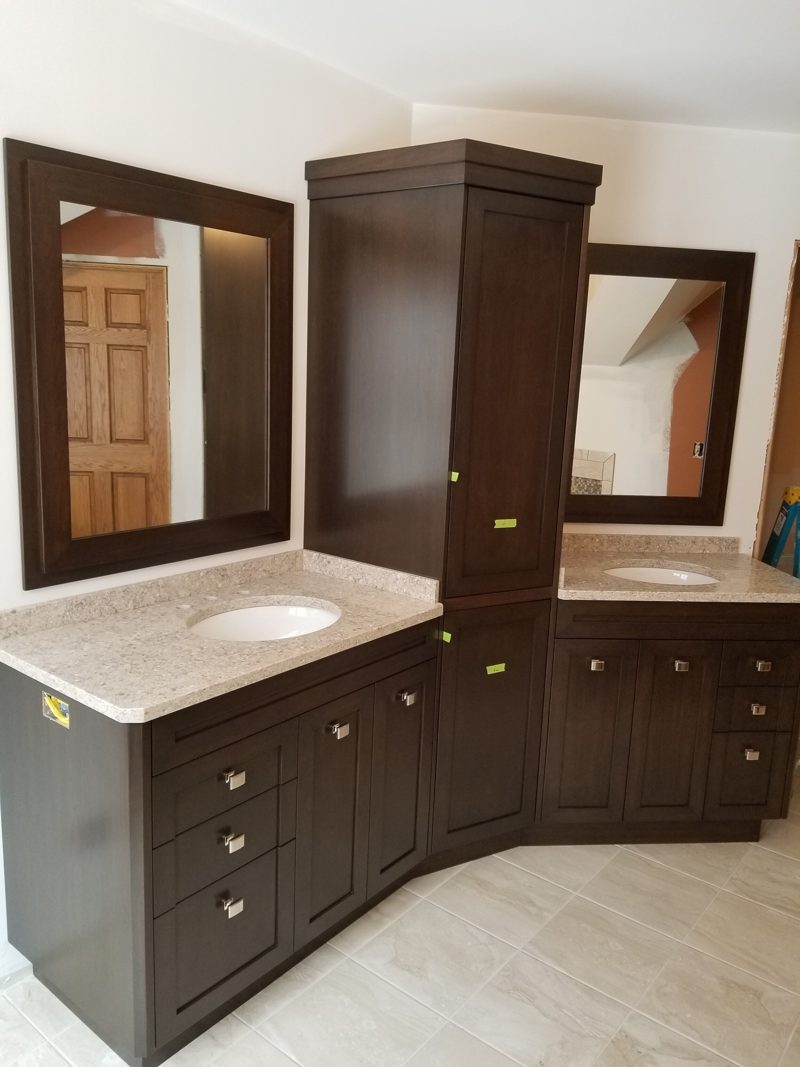 Corner espresso vanity with a center linen tower, stone countertops, and framed mirrors