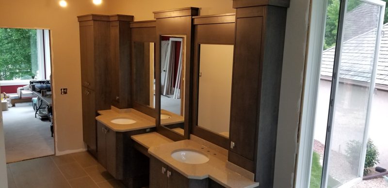 Long gray vanity with tall towers, framed mirrors, and a window at the end