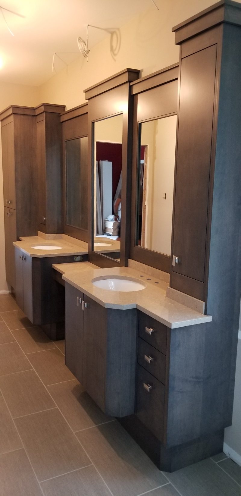 Tall gray wood towers framing mirrors above a stone-topped vanity
