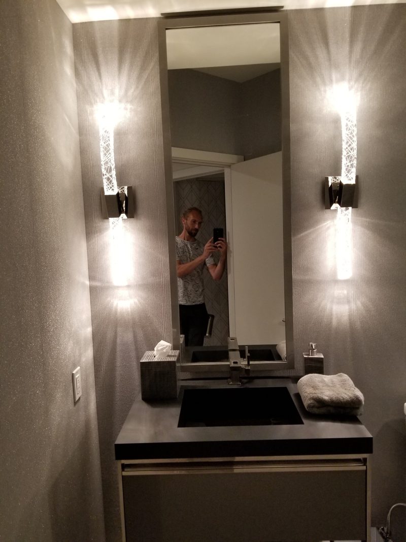 Powder room with a dark vanity, tall mirror, and glass wall sconces
