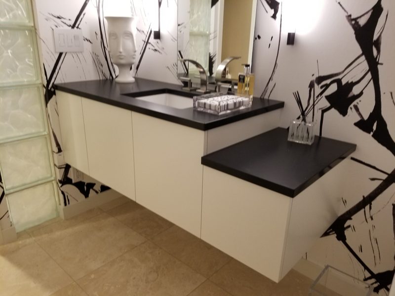 Floating white vanity with a wraparound black top beside a glass block wall