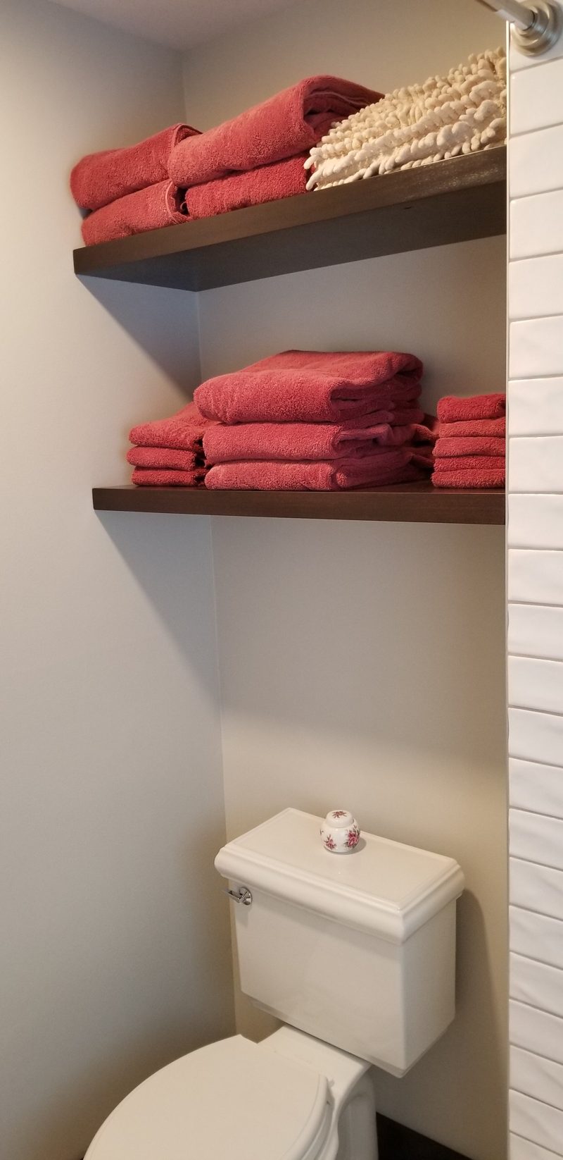 Floating dark wood shelves holding red towels above a toilet