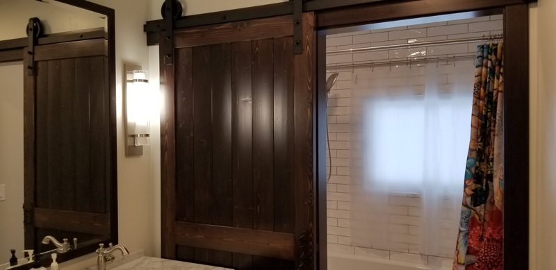 Rustic dark wood sliding barn doors beside a mirror and a shower