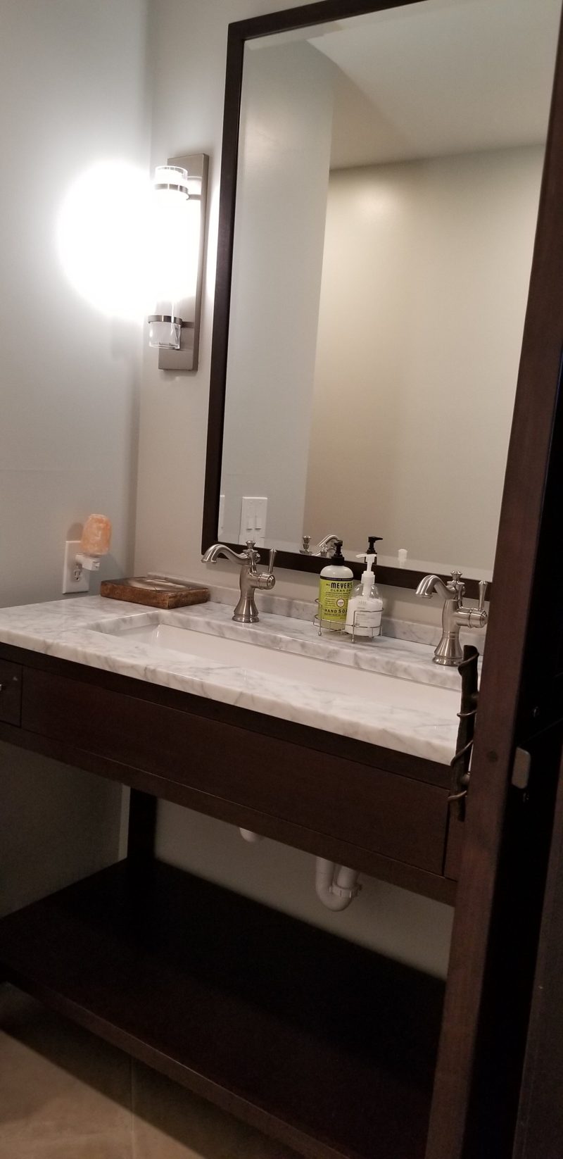 Open dark wood vanity with a marble top below a tall framed mirror