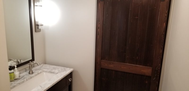 Dark plank barn door beside a marble-topped vanity and framed mirror