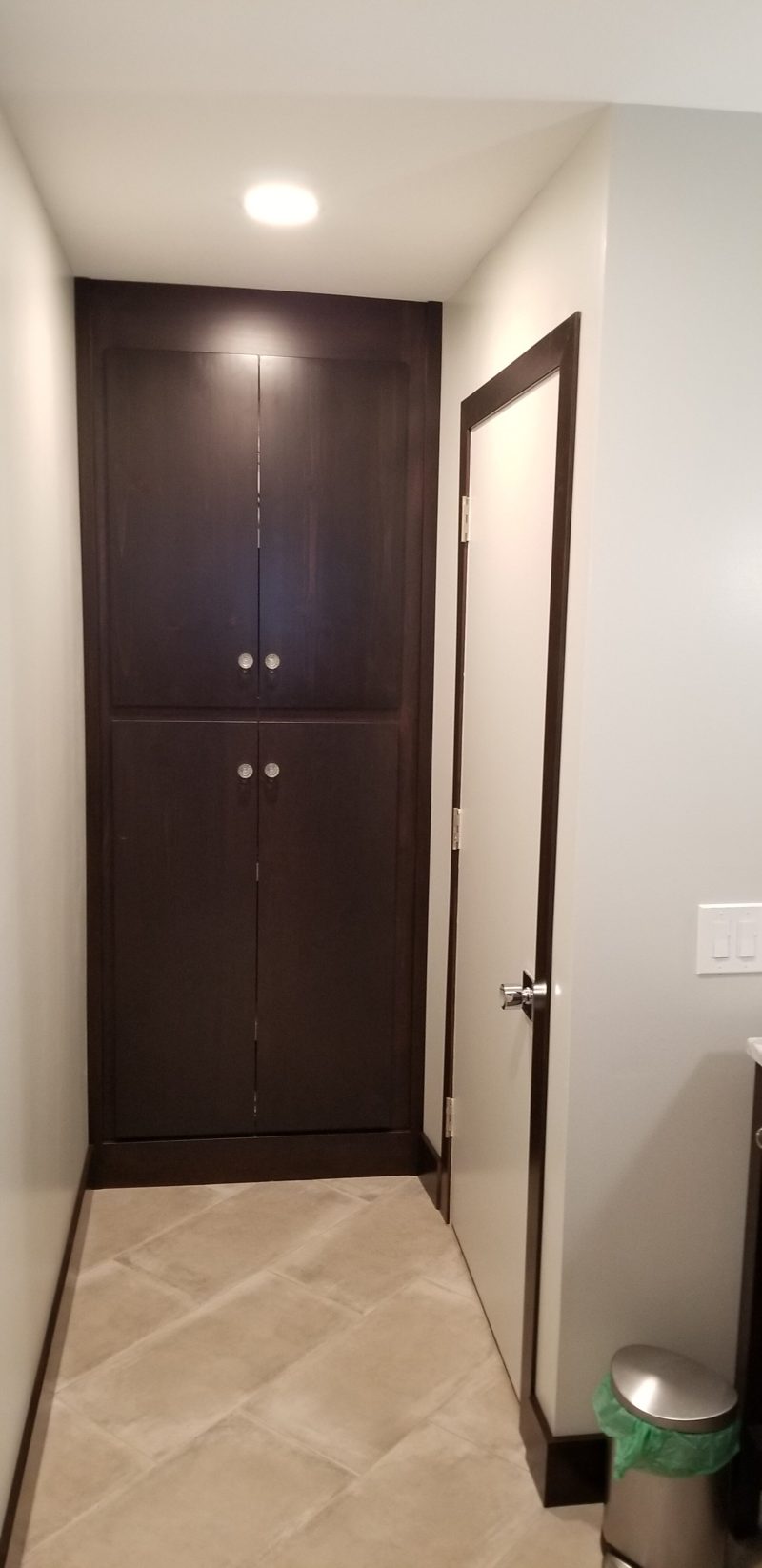 Tall dark wood linen cabinet with paneled doors at the end of a hallway