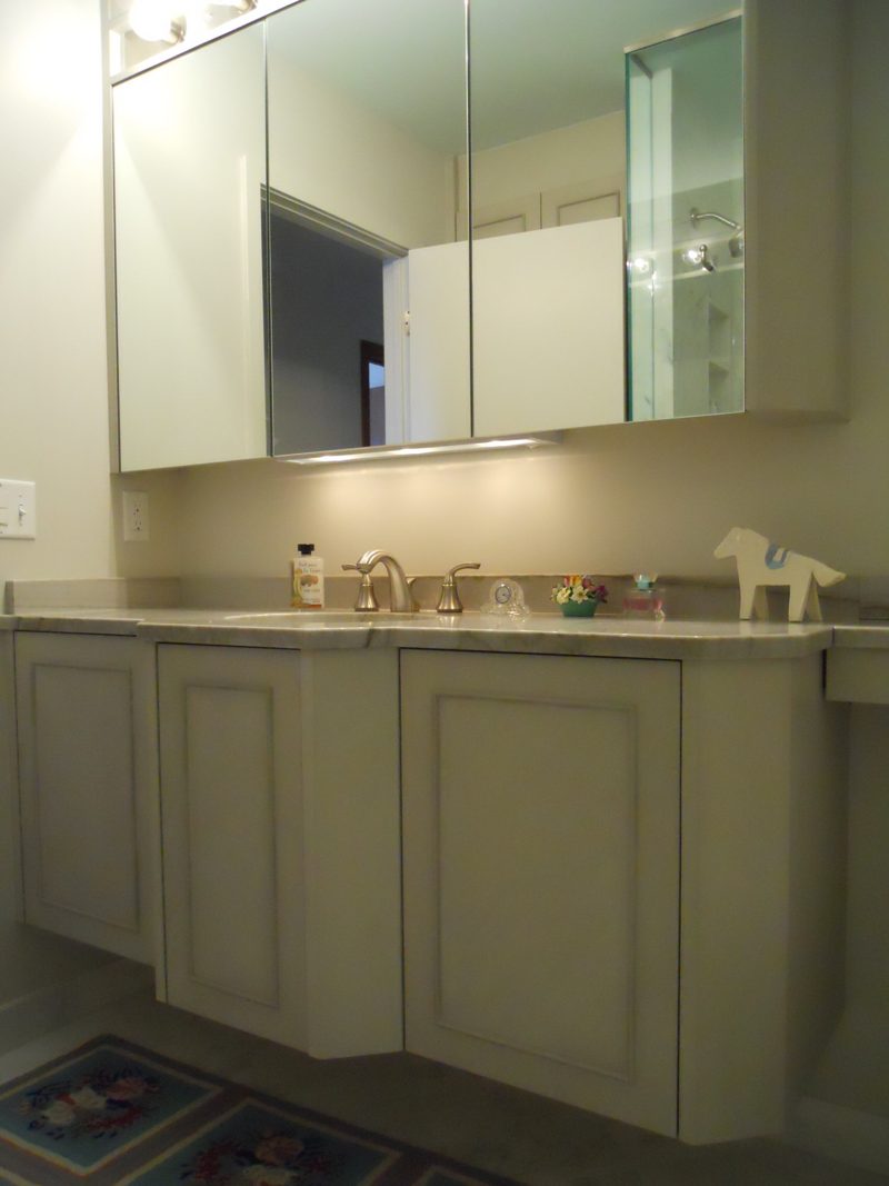 Gray painted vanity with raised panel doors below a large mirrored medicine cabinet