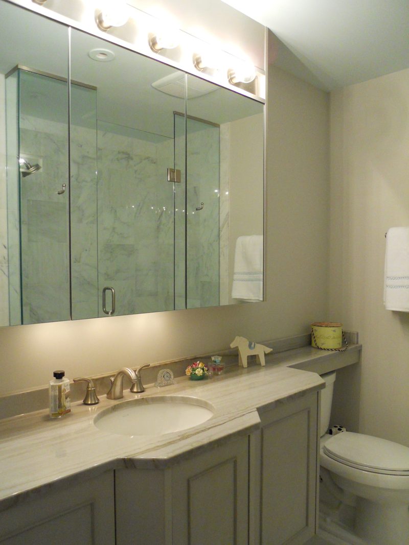 Gray vanity with a marble countertop, medicine cabinet, and glass shower beside it