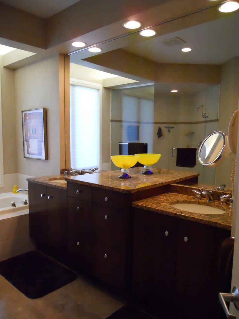 Dark wood double vanity peninsula with granite top and a mirrored wall