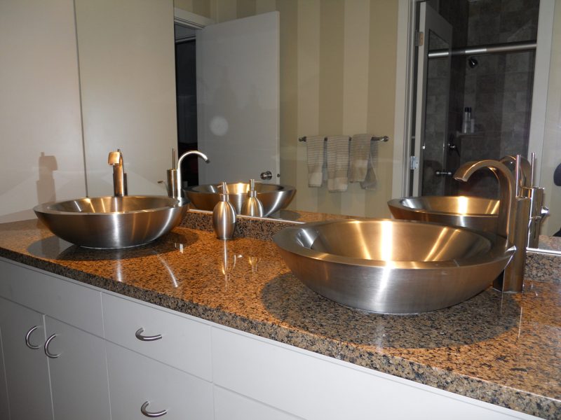 Stainless steel vessel sinks on a speckled granite top over white cabinets