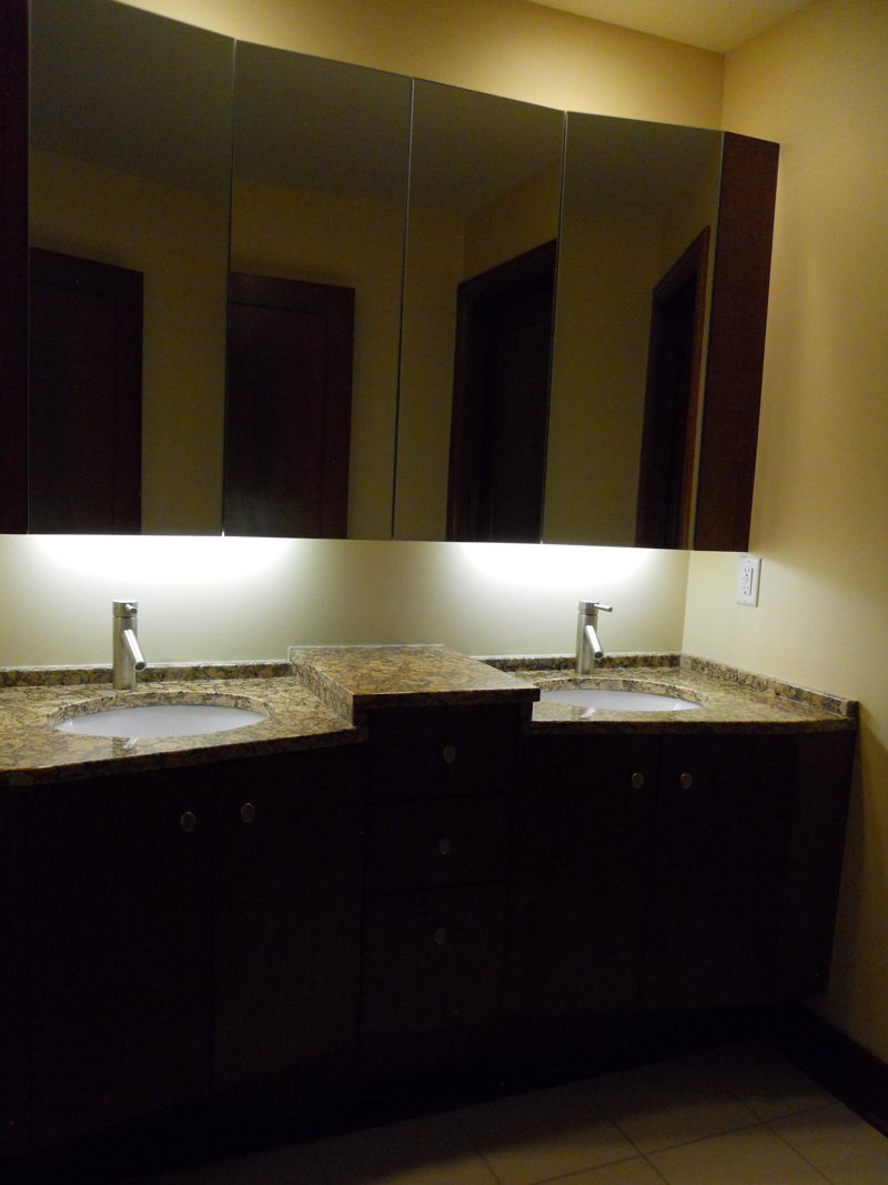 Dark wood double vanity with a granite top and under-cabinet lighting