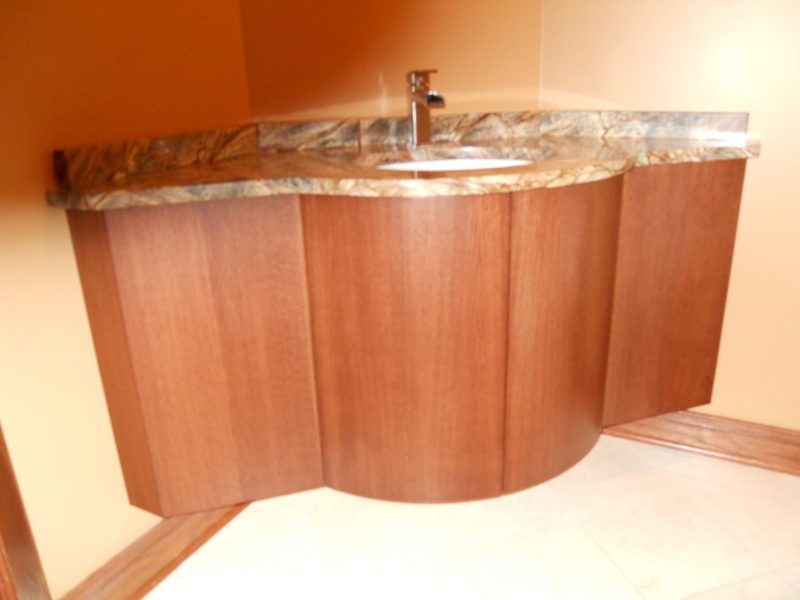 Curved light wood floating vanity with a thick stone countertop