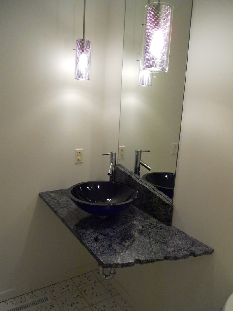 Wall-mounted granite shelf with a dark glass vessel sink and pendant lights
