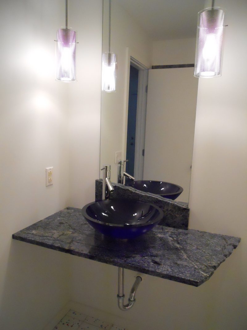 Floating stone counter with a blue glass vessel sink below pendant lights