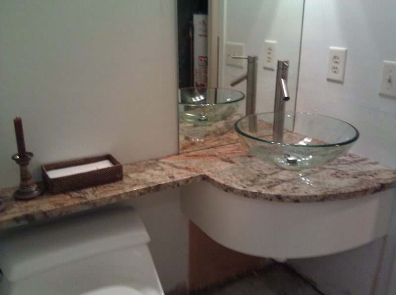 Curved granite vanity with a glass vessel sink and a white base