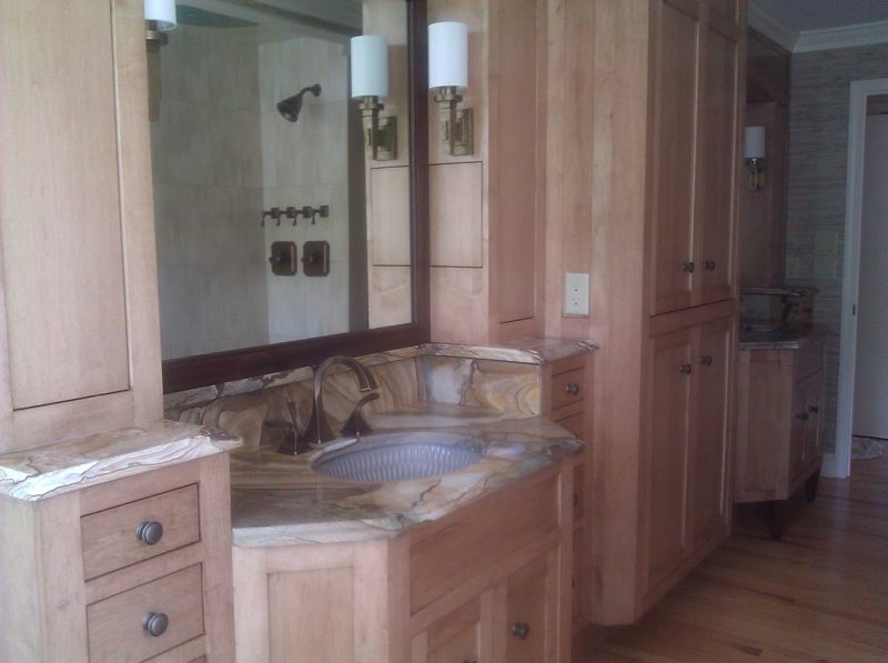 Light wood vanity with stone countertop, framed mirror, and tall linen cabinet