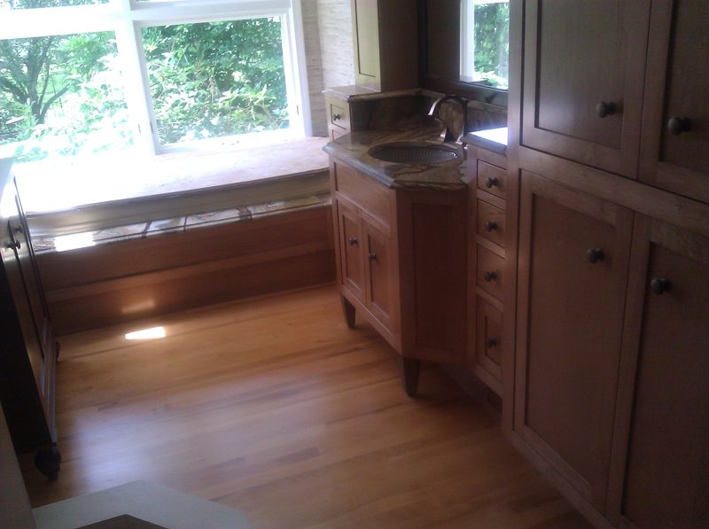 Light wood vanity cabinetry and window seat in a bathroom with wood floors