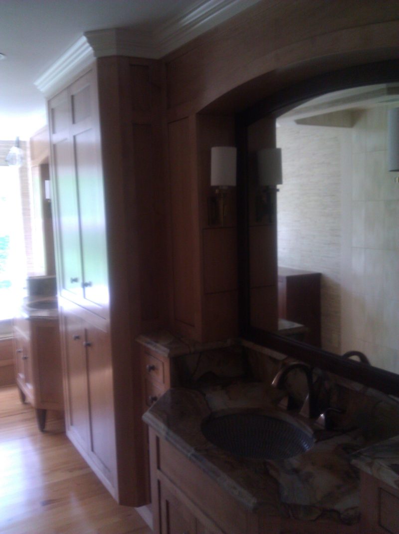 Arched mirror surround with a dark granite vanity and tall wood cabinetry