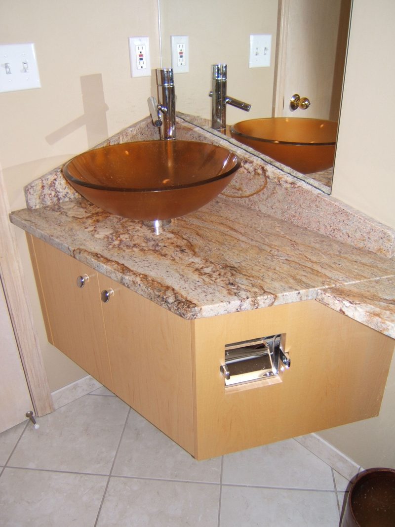 Maple corner vanity with an amber glass vessel sink on a granite top, seen from above