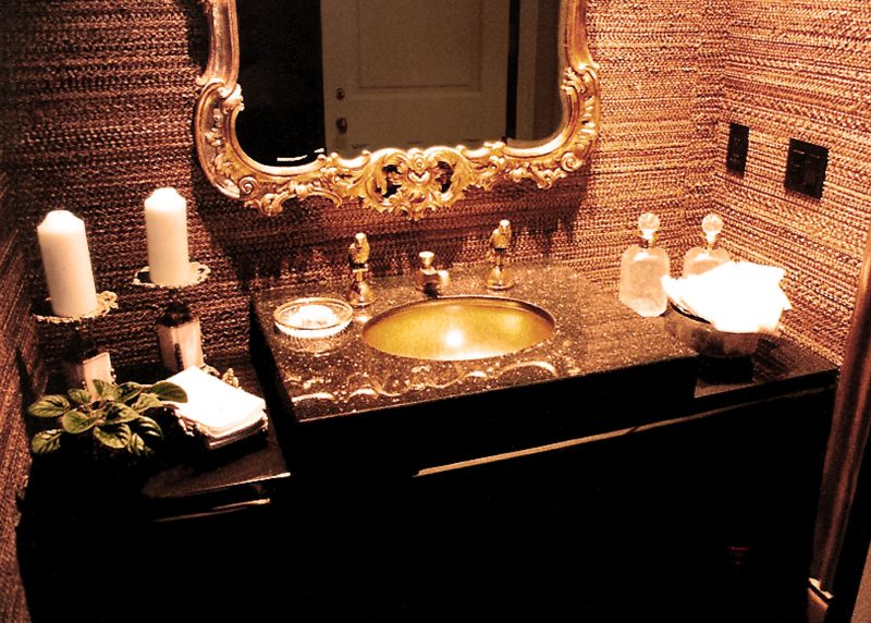 Dark vanity with a gold sink and ornate gold framed mirror in a textured powder room
